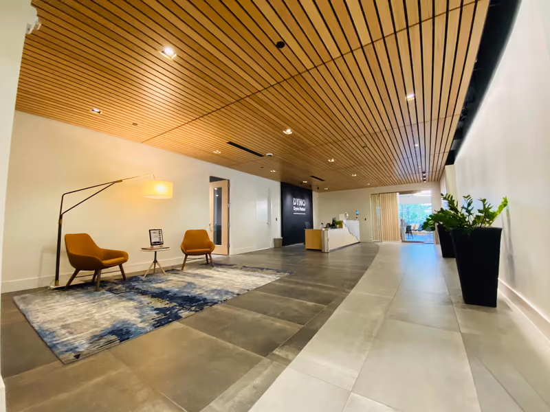 The completed Dyno Nobel office lobby — lounge seating on a patterned rug beneath a warm slatted wood ceiling, with the reception desk beyond