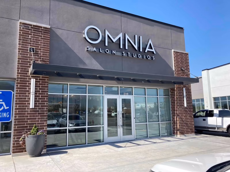 The completed Omnia Salon Studios storefront in Pleasant Grove — brick piers flanking a full-height glass entry beneath a dark sign band and steel awning